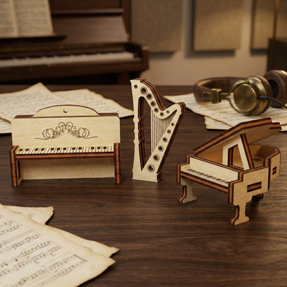 Laser cut plywood miniatures of a grand piano, an upright piano with floral engraving, and a tall harp. The 3D wooden models stand upright on a desk surrounded by music sheets, showing precise layered edges and light wood texture.