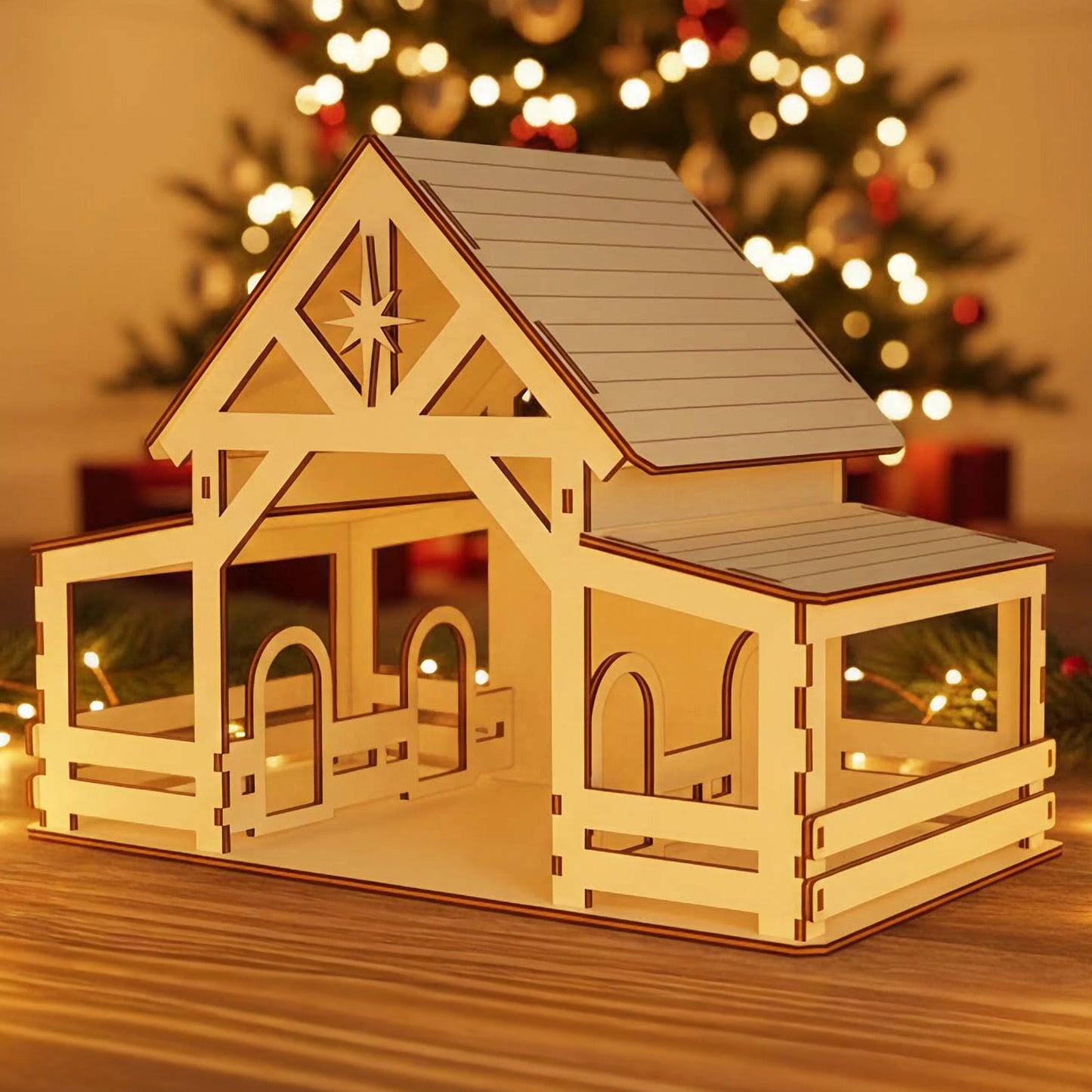 
Wooden laser cut Nativity barn #5 with extended covered porch, detailed beam structure, and prominent Bethlehem star cutout on the gable, illuminated warmly against a softly blurred Christmas tree background.