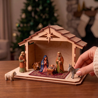 Hand sets a toy donkey beside a laser cut plywood nativity stable and holy family figures on a wood table near a lit tree.
