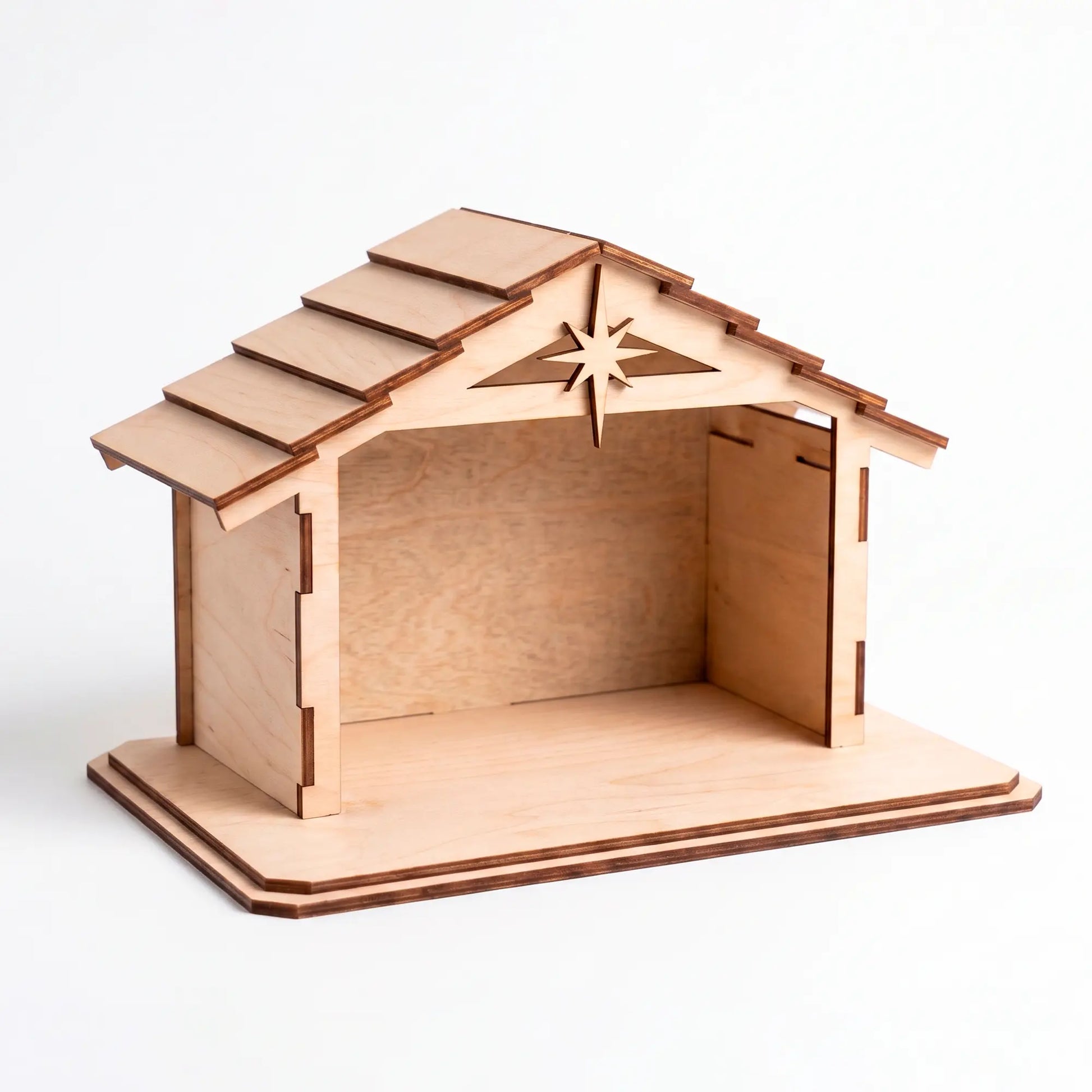 Front view of an empty laser cut plywood nativity stable showing detailed roof shingles and a star on a white background