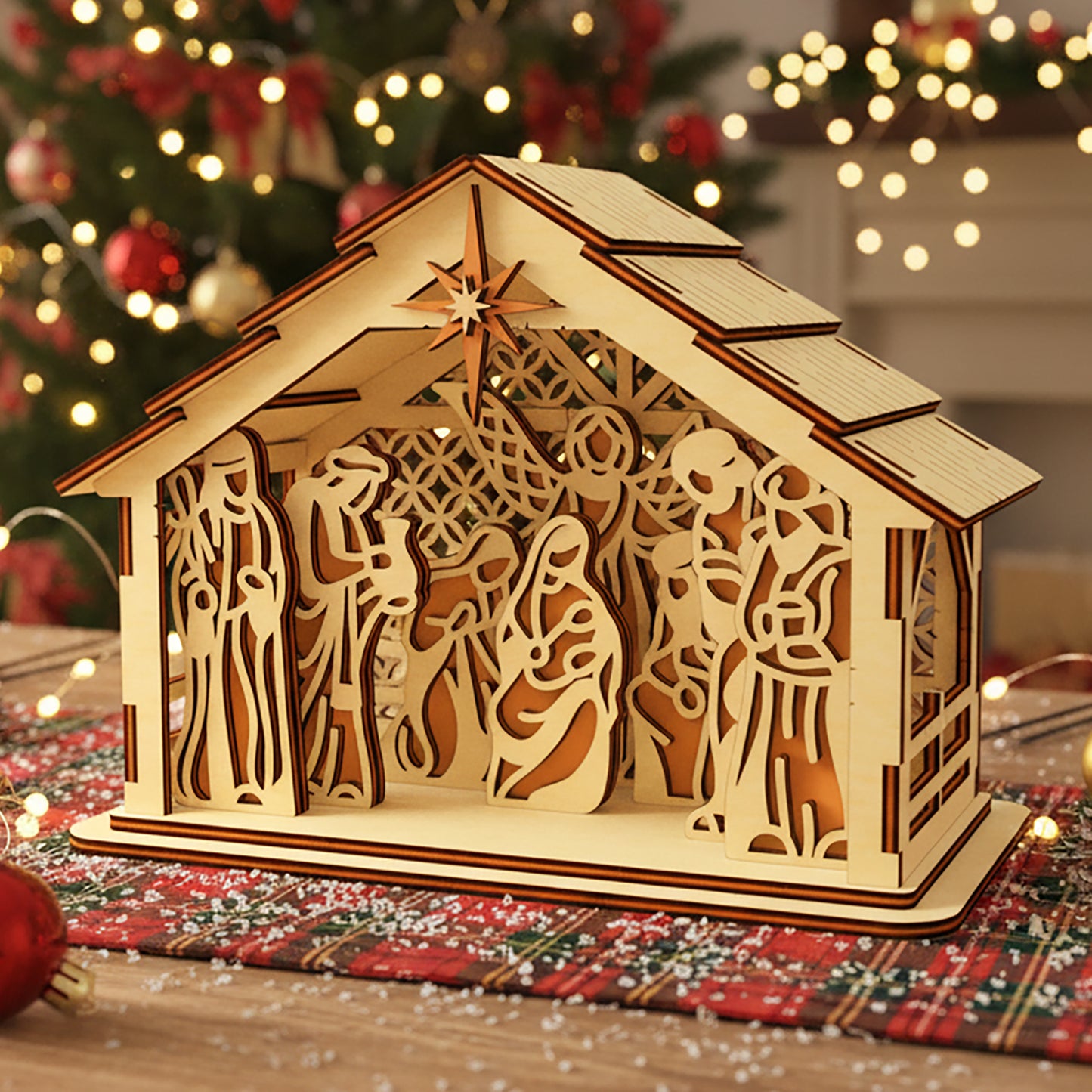 Laser cut wooden 3D Nativity scene with layered Mary, Joseph, baby Jesus and Bethlehem star, illuminated from within against a warm Christmas tree bokeh background.