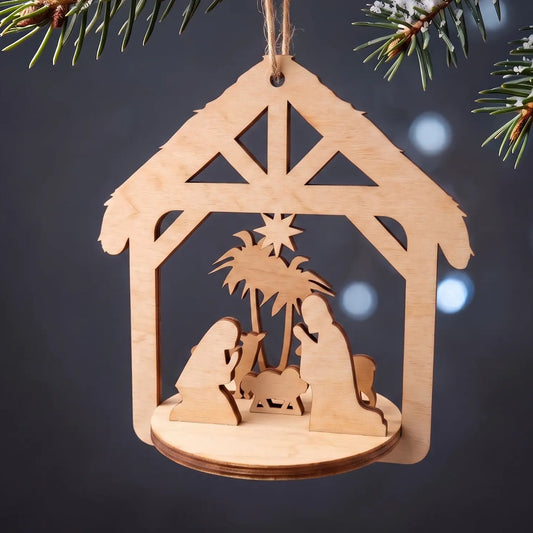Laser cut plywood nativity scene ornament hanging from snowy evergreen bough against glowing bokeh lights.