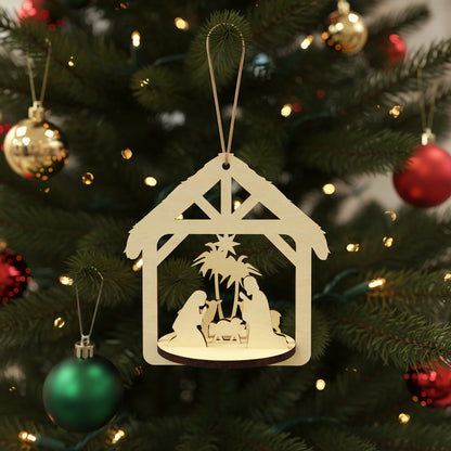 Delicate laser cut Nativity scene featuring a detailed Holy Family manger scene framed in a rustic stable shape with hanging loop, set against a festive lighted Christmas tree background.