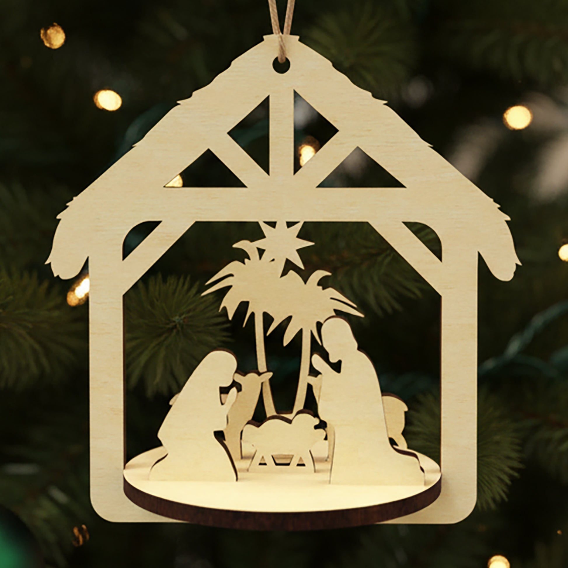Laser cut wooden Nativity scene with layered silhouettes of Mary, Joseph, baby Jesus, palm trees and Bethlehem stable under a thatched roof, displayed against a twinkling Christmas tree background.