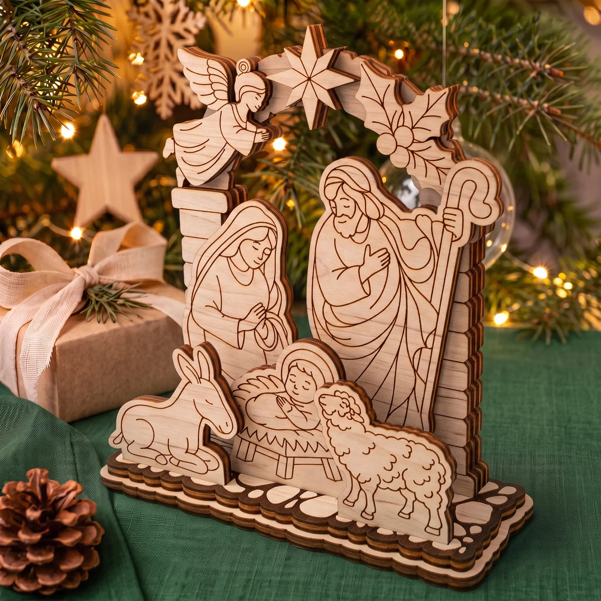 Side angle of laser cut plywood layered nativity set on holiday table with pine branch and gift box.