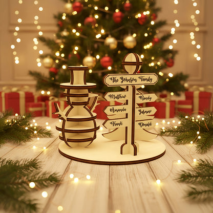 Personalized laser cut wooden North Pole signpost with family member names next to a cheerful snowman figure, shown on a warm bokeh-lit holiday background.