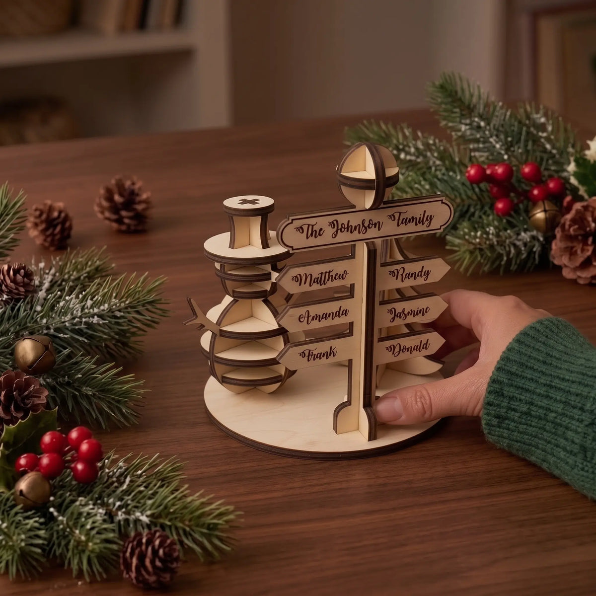 Hand places personalized laser cut plywood North Pole family signpost table centerpiece near holiday greenery