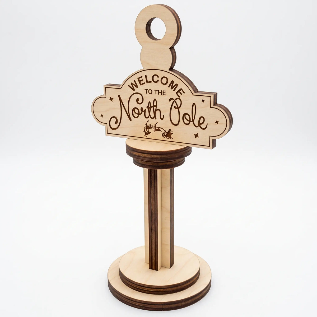 Horizontal laser cut plywood Welcome to the North Pole post ornament on stepped wooden base against white background.