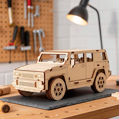 Laser cut wooden plywood 3D model sitting on a slate mat in a workshop setting. Detailed plywood puzzle assembly featuring a textured front grille, round headlights, and realistic tires. Background shows a pegboard with tools and a warm desk lamp.
