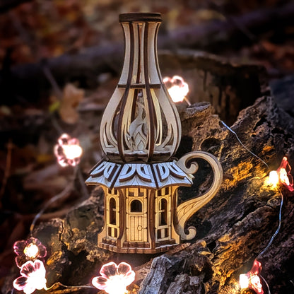 Wooden oil-lamp shaped fairy house made from laser-cut plywood, displayed outdoors on a tree stump with warm glowing lights