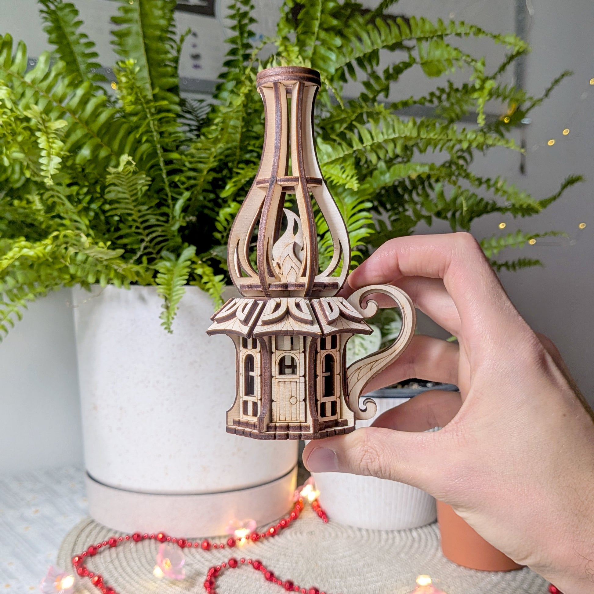 Hand holding a small wooden fairy house shaped like an oil lamp, showcasing the scale and laser-cut details