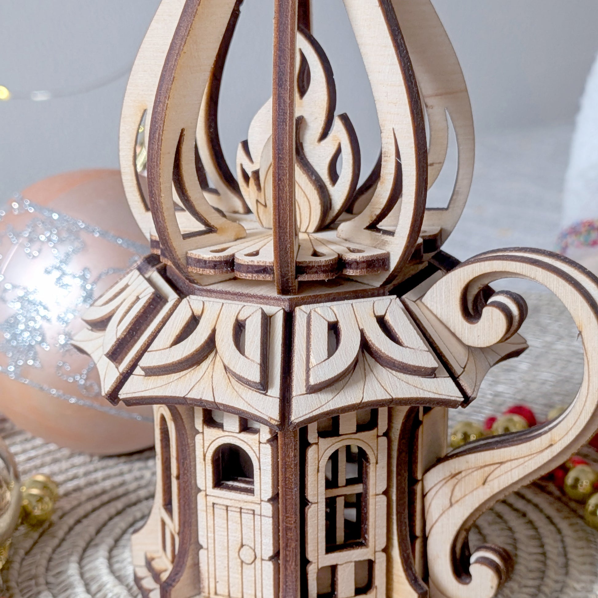 Close-up of the laser-cut wooden oil-lamp fairy house, highlighting intricate flame and curved structural design