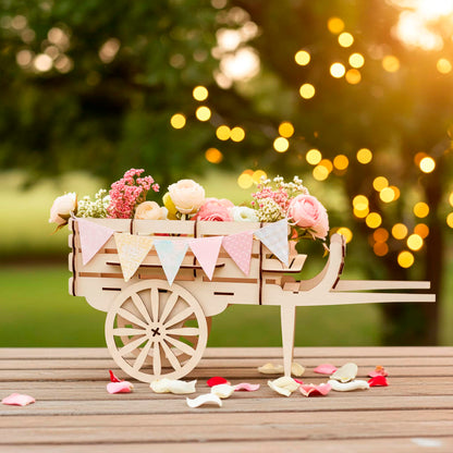 Laser cut wooden plywood miniature cart used as a planter, filled with soft pink roses and decorated with a colorful triangle bunting, set on a wooden deck during a golden sunset.