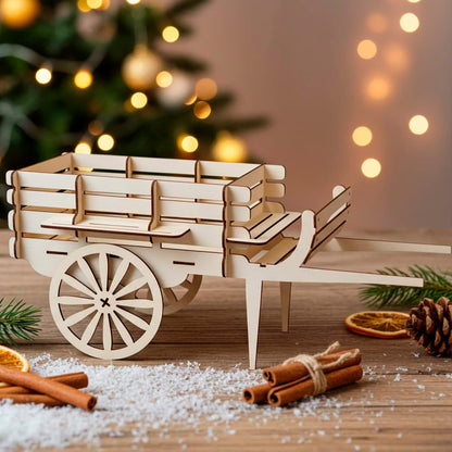 A light brown laser cut wooden plywood miniature wagon sitting on a wooden table with faux snow, cinnamon sticks, and dried orange slices, with a glowing Christmas tree in the blurred background.