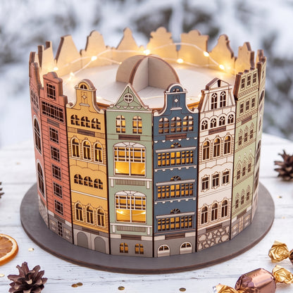 Illuminated laser cut plywood old town candy box glowing on snowy wooden table with pinecones, lights, and sweet treats.