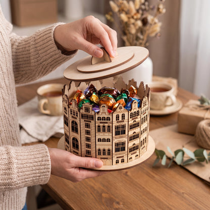 Woman opening a laser cut plywood old town candy box filled with wrapped chocolates on a cozy wooden tea table with cups.