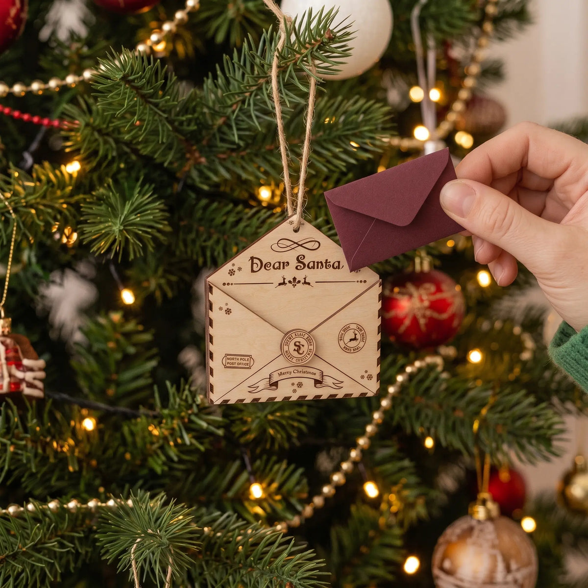 Laser cut plywood Dear Santa envelope ornament hanging on Christmas tree with hand holding mini letter.