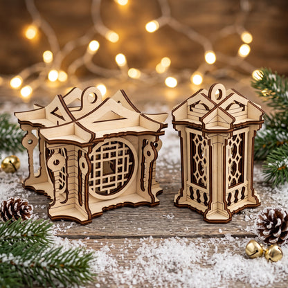 Two different laser cut plywood lantern ornaments placed on a snowy surface with pine cones and golden bells.