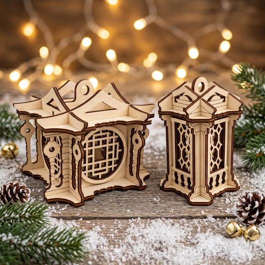 Two different laser cut plywood lantern ornaments placed on a snowy surface with pine cones and golden bells.