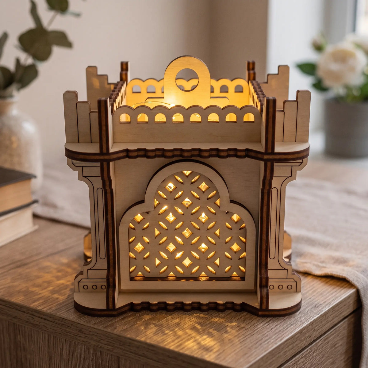 Illuminated cubic laser cut plywood lantern with castle battlements and warm glowing geometric lattice on wooden sideboard.