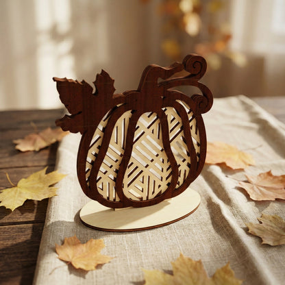 Decorative pumpkin crafted from laser cut plywood with a bold diagonal lattice pattern. The dark brown top layer and light wood bottom layer provide a rich contrast. Surrounded by dried autumn leaves on a rustic wooden table.