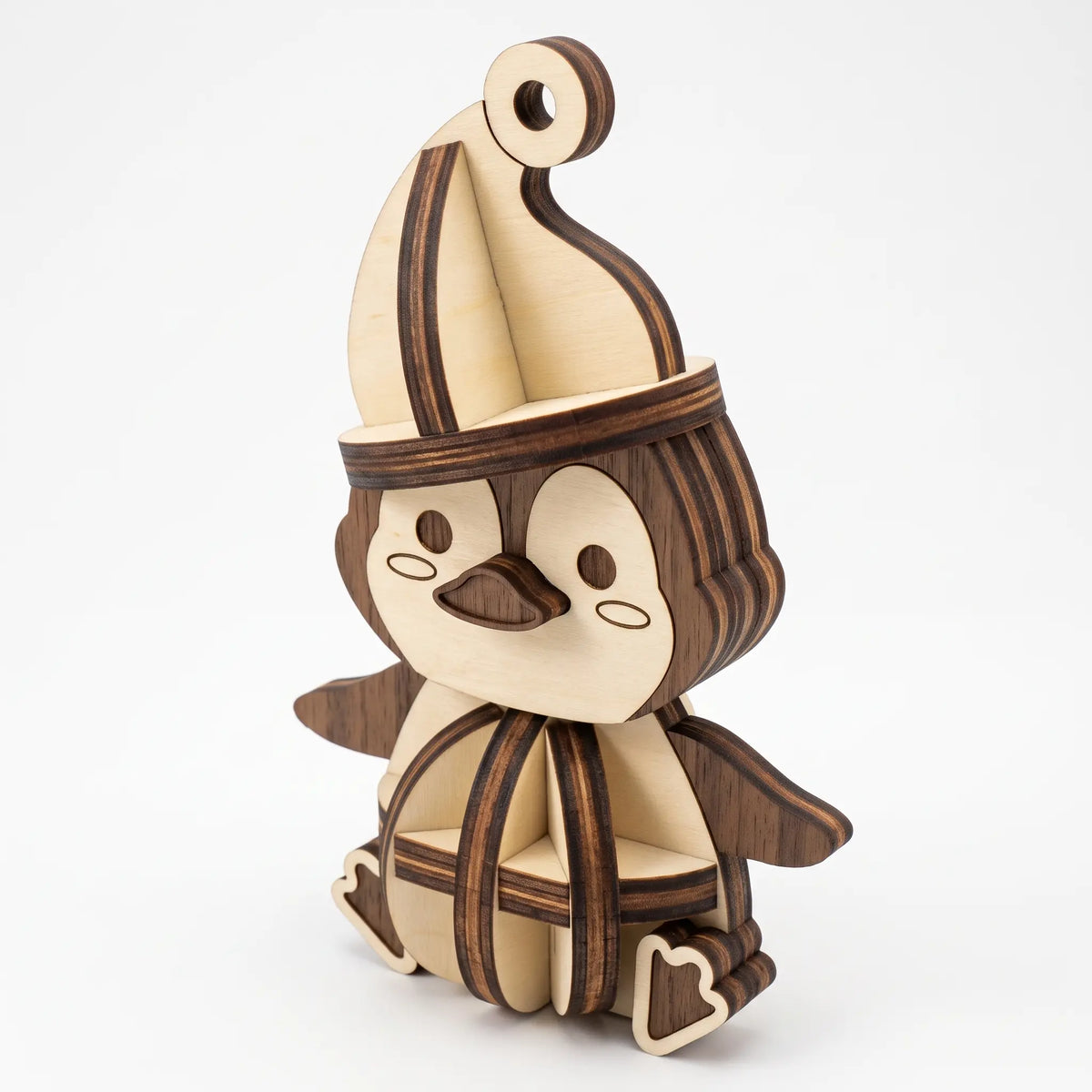 Three-quarter view of laser cut plywood penguin figurine showing 3D slotted spherical body on seamless white background.