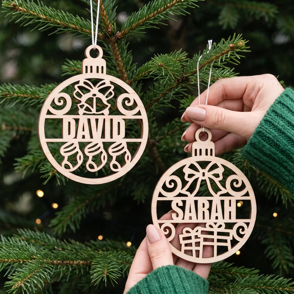 Hands display personalized laser cut plywood name baubles David and Sarah on an illuminated pine Christmas tree
