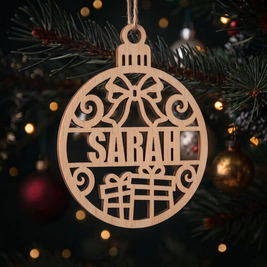 Laser cut plywood Sarah name bauble ornament with bow and gifts hanging from fir branches with warm bokeh lights.