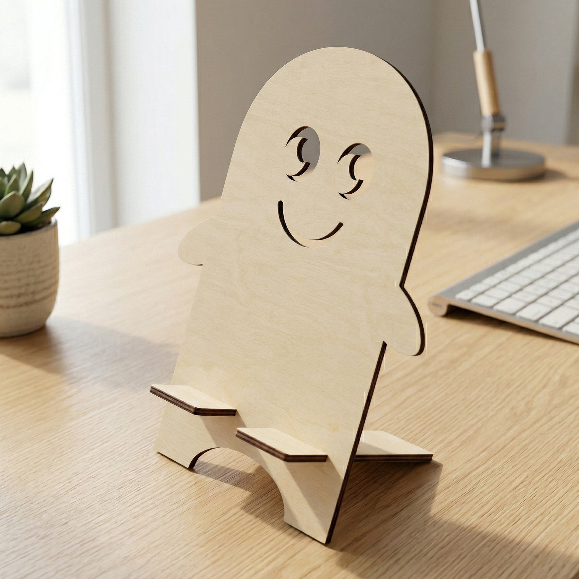 Close-up of a handcrafted laser-cut plywood phone holder in the shape of a friendly character. The image highlights the natural wood grain, dark burnt edges, and the sturdy interlocking support mechanism. Posed on a minimalist office desk in bright natural light.