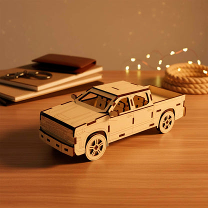 Laser cut wooden plywood 3D puzzle of a pickup truck. Detailed front view showing the grill, headlights, and bumper. The model is made of light plywood with dark burnt edges, resting on a wooden table next to books and leather notebooks.