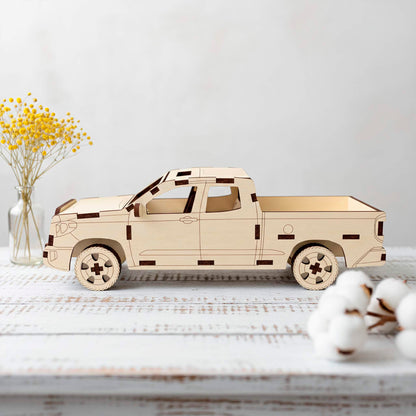 Side profile of a laser cut wooden plywood pickup truck 3D puzzle model. The detailed craft is displayed on a white rustic table next to a vase of yellow dried flowers and soft cotton bolls, highlighting its clean lines and precise assembly.