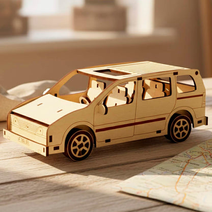Three-quarter front view of a laser cut wooden plywood assembly kit. The 3D wood puzzle features a detailed grill, headlights, and side mirrors. Displayed in a bright room on a wooden table next to travel gear and a map.