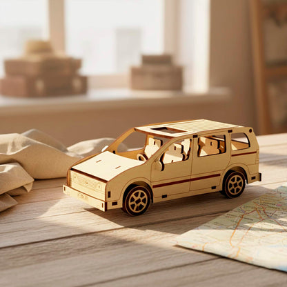Three-quarter front view of a laser cut wooden plywood assembly kit. The 3D wood puzzle features a detailed grill, headlights, and side mirrors. Displayed in a bright room on a wooden table next to travel gear and a map.