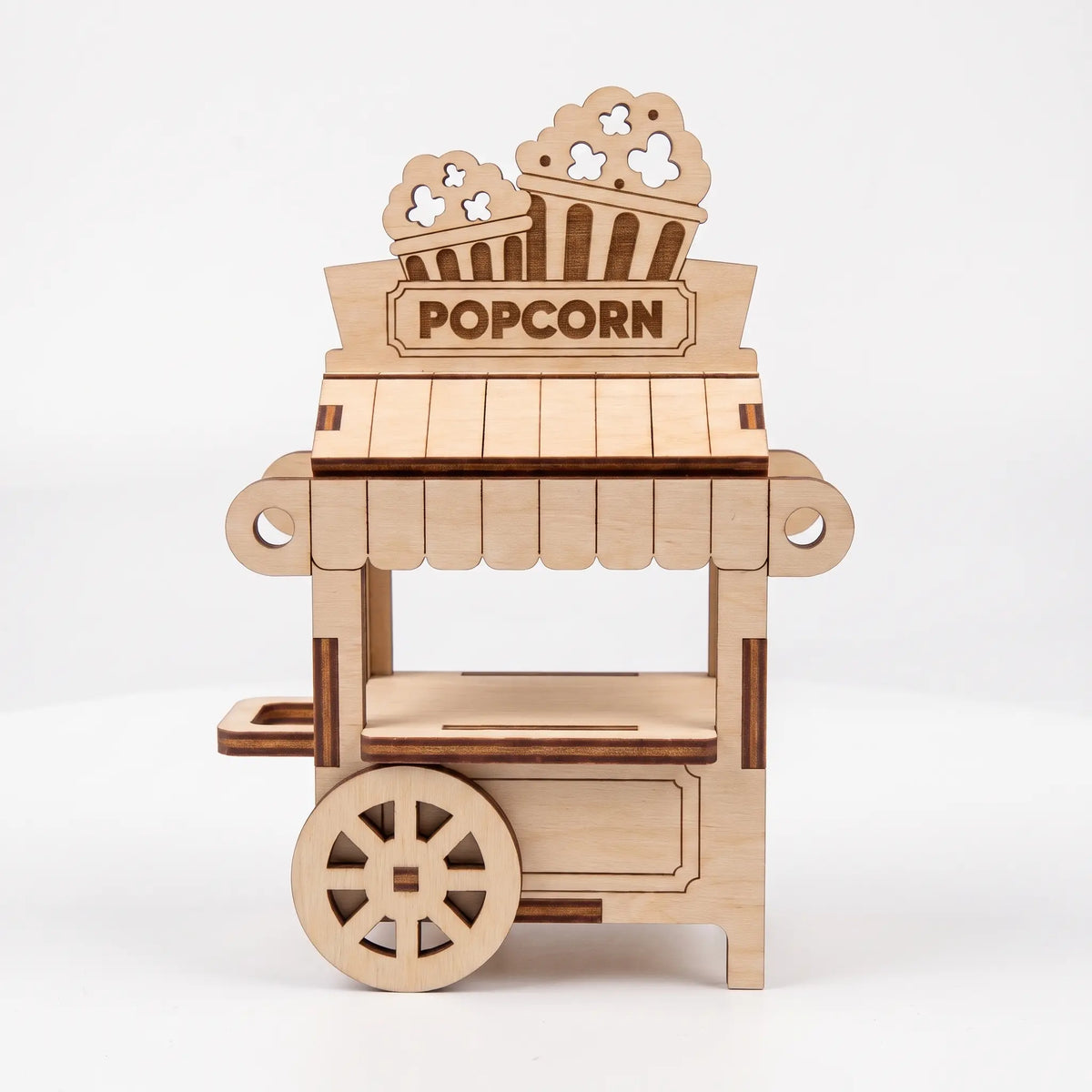 Front view of 3D laser cut plywood popcorn cart model with spoked wheel, striped canopy, and sign on plain white backdrop.