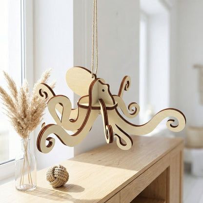 A whimsical 3D octopus ornament made of laser cut plywood, hanging from a twine string. The interlocking wooden pieces create a dynamic shape with curled tentacles. Displayed in a bright, modern interior near a window with pampas grass.