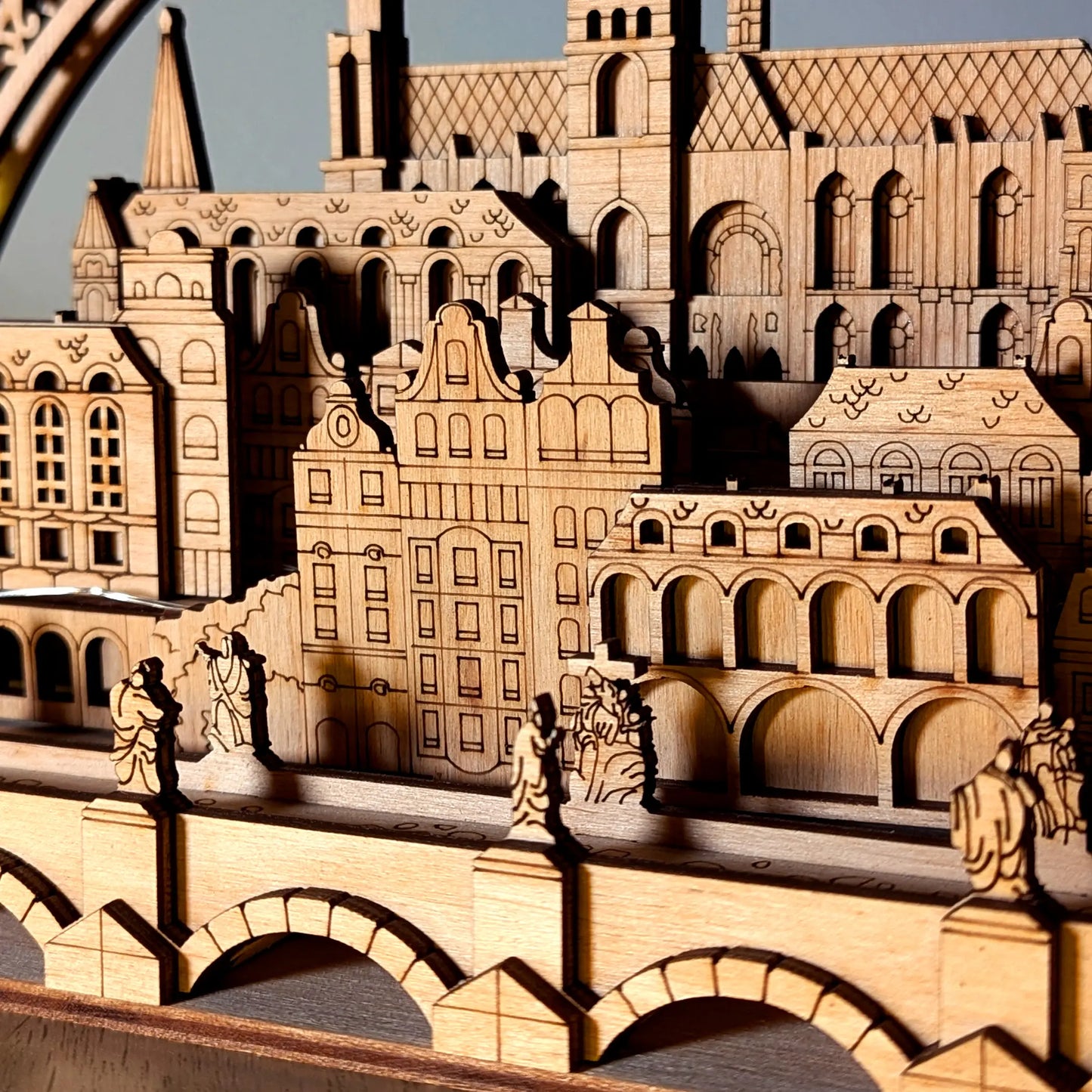 A detailed macro shot of miniature historical bridge statues in front of Prague old town facades made from laser cut plywood.