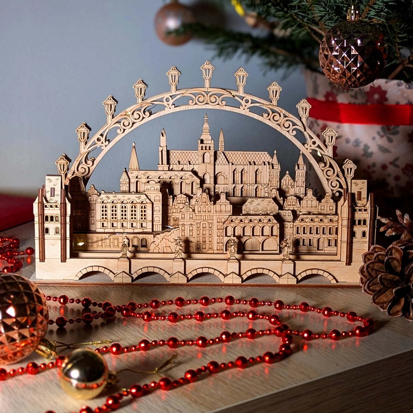 Atmospheric product photography of a glowing 3D Prague village silhouette arch display beautifully made of laser cut plywood.