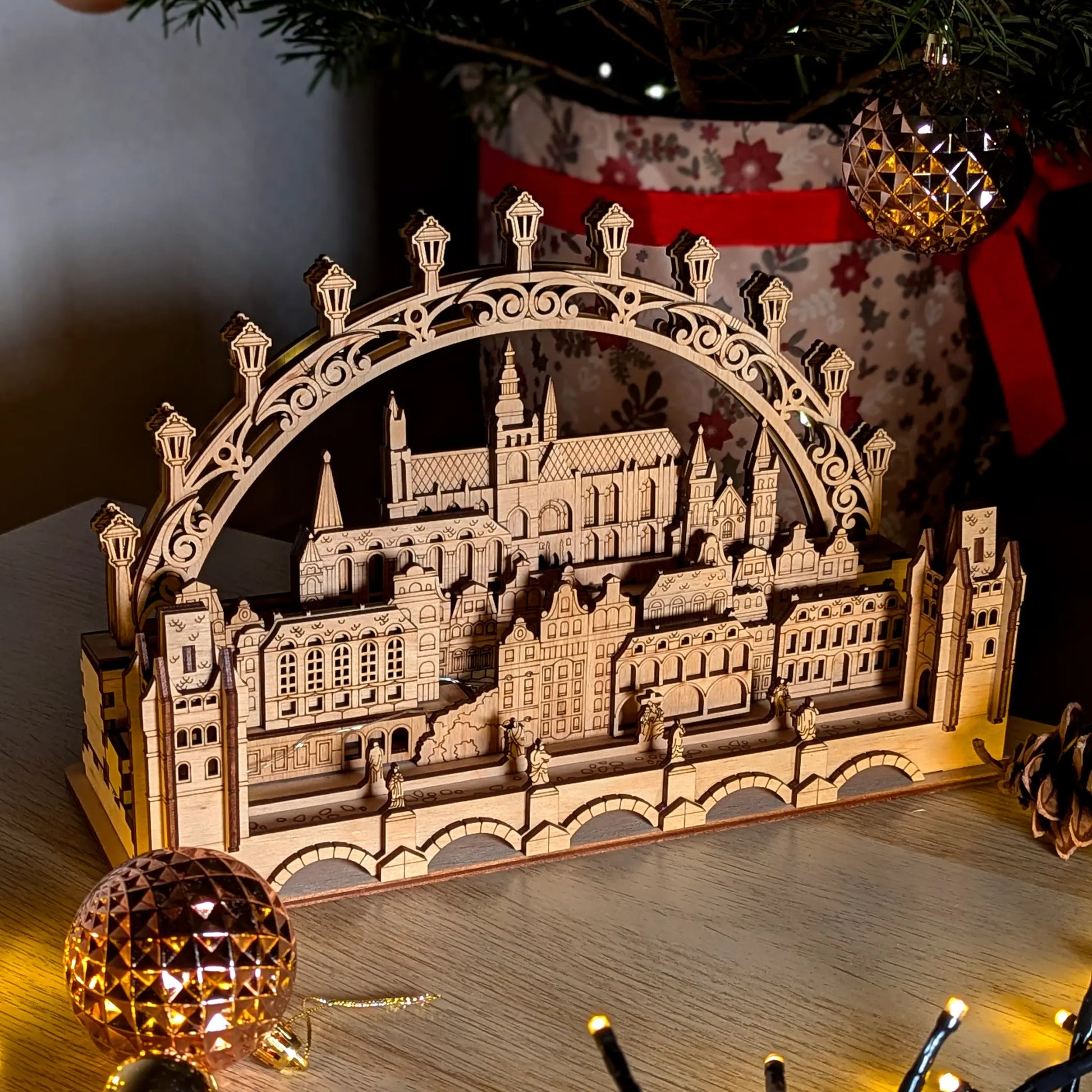 A cozy angled perspective view of an illuminated miniature Prague cityscape silhouette arch made from laser cut plywood.