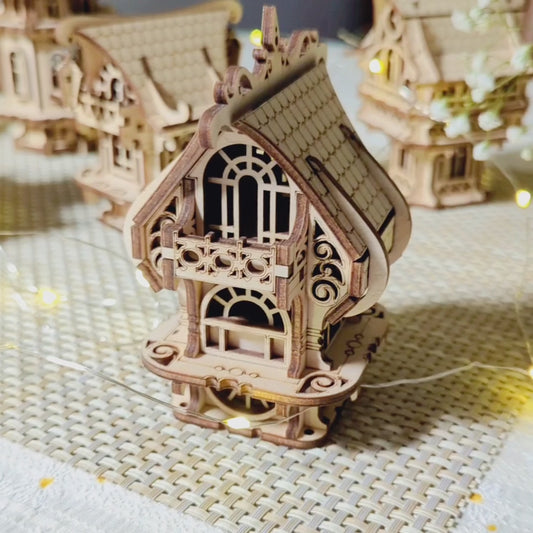 A collection of five miniature laser cut plywood buildings displayed next to a beautiful pink flower bouquet indoors.