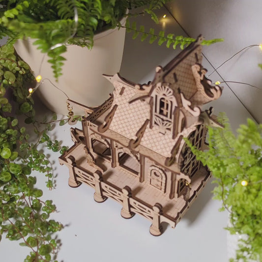 Atmospheric product photography of a 3D miniature lighthouse puzzle styled near flowers with laser cut plywood.