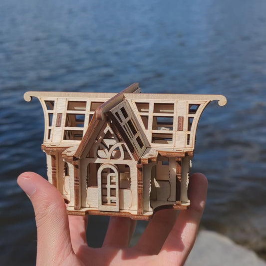 Laser cut plywood miniature orangery structure with geometric window panels on natural rock surface.