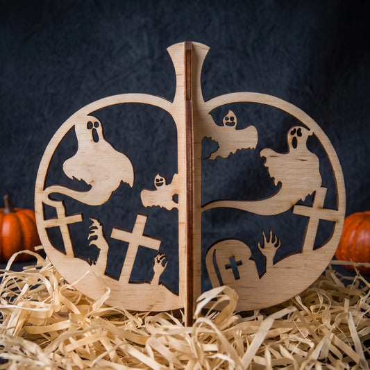A wooden  laser citHalloween Pumpkin with ghost, cross, hand, and tombstone motifs, displayed on a bed of shredded paper