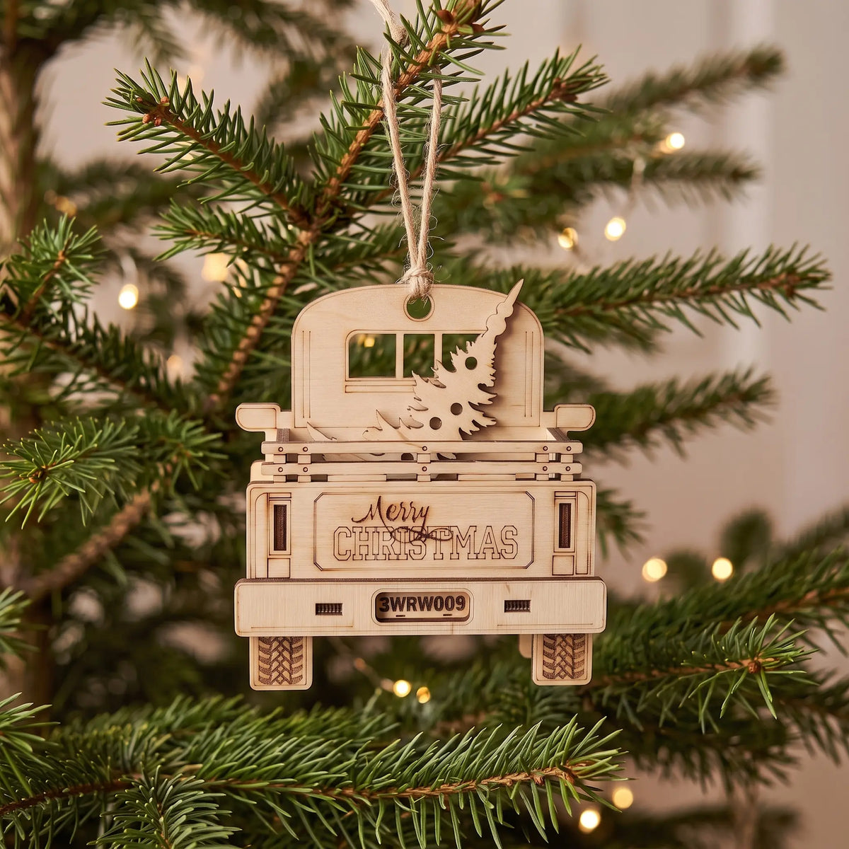 Rear view of a laser cut plywood holiday pickup truck ornament hanging on Christmas tree with warm lights.