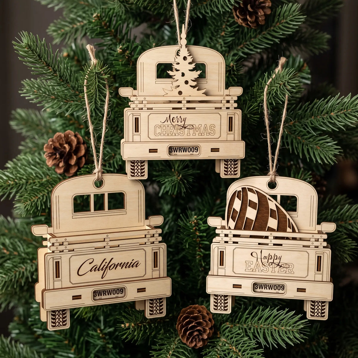 Three laser cut plywood truck ornaments with tree, egg, and custom text hanging on pine branches with cones.