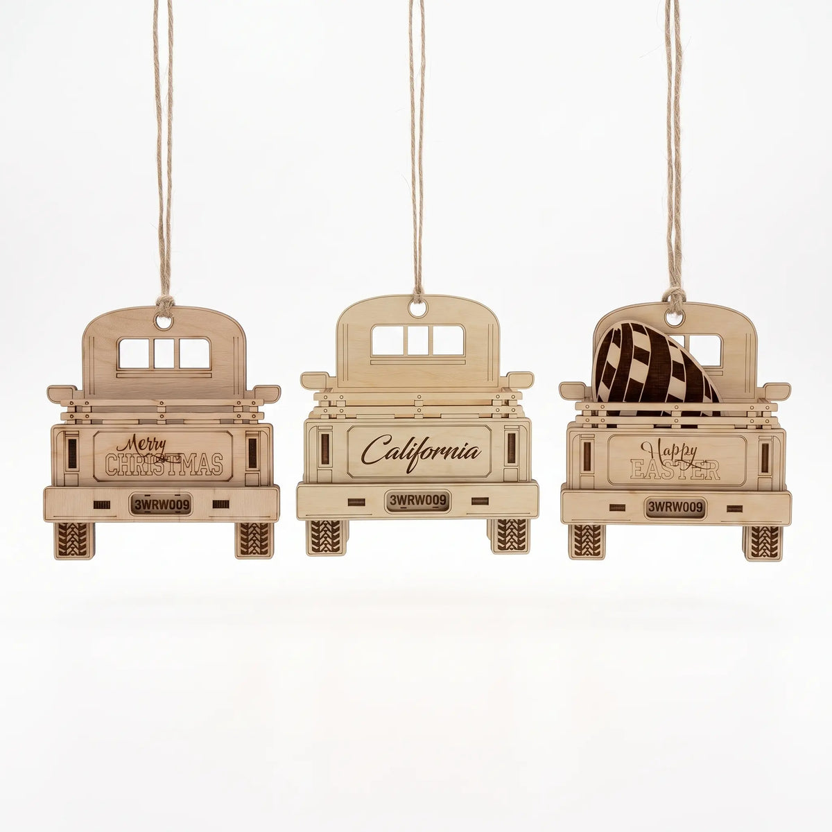 Set of three laser cut plywood pickup truck ornaments hanging on jute twine, isolated on white background.