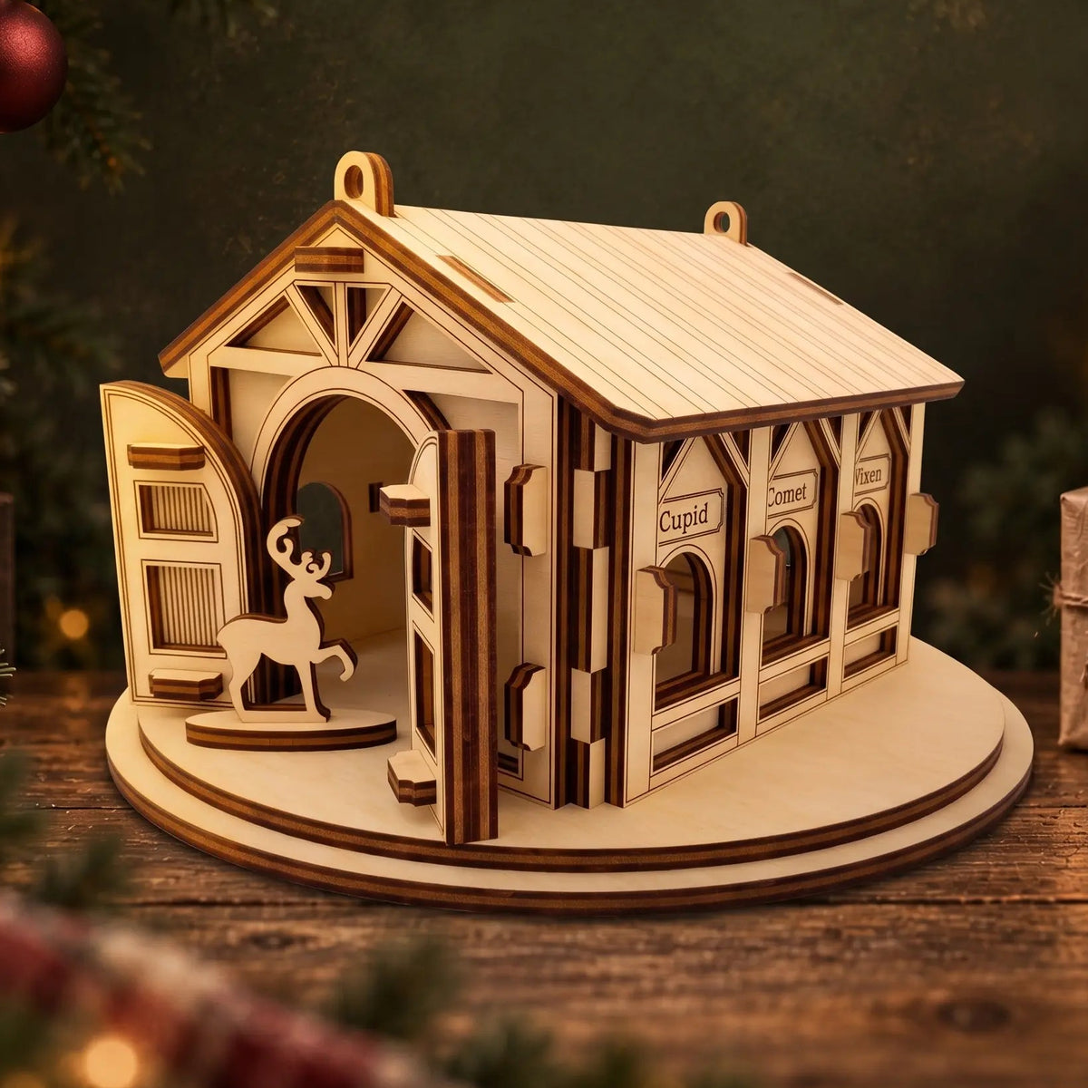 Laser cut plywood reindeer barn with open front doors and engraved feeding stalls on dark wood festive tabletop