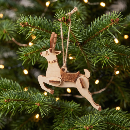 Close-up of a laser cut plywood reindeer ornament hanging on pine Christmas tree with warm glowing holiday lights behind.