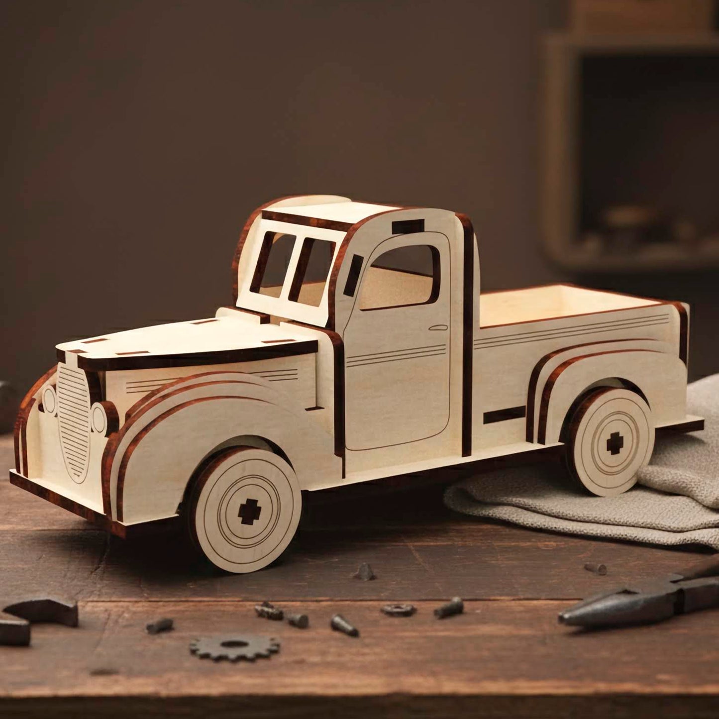 Laser cut wooden plywood retro pickup truck model with a vintage rounded design. Plywood 3D puzzle resting on a wooden workbench surrounded by tools like wrenches and pliers. Features layered fenders, a front grill, and a classic cabin shape