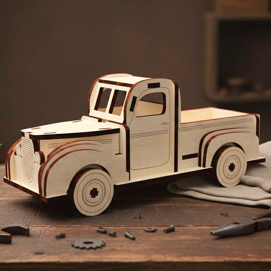 Laser cut wooden plywood retro pickup truck model with a vintage rounded design. Plywood 3D puzzle resting on a wooden workbench surrounded by tools like wrenches and pliers. Features layered fenders, a front grill, and a classic cabin shape