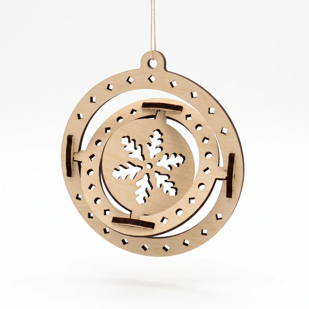 Spun laser cut plywood 3D sphere ornament showing rotating rings with cutout snowflake on white background.